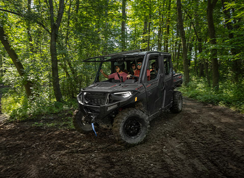 A black Polaris RANGER XP 1000UTV with a full cab and four people enjoying a trail ride through a sun-dappled, green forest.