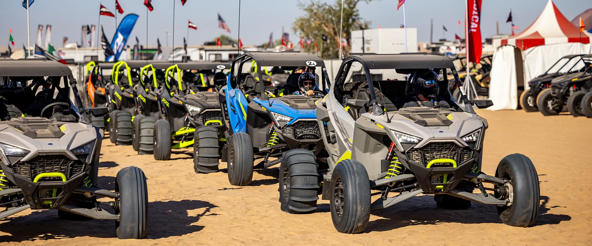 Helmeted riders drive a lineup of Polaris RZR off-road vehicles across the sand at Camp RZR.