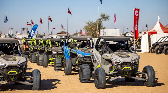 Helmeted riders drive a lineup of Polaris RZR off-road vehicles across the sand at Camp RZR.