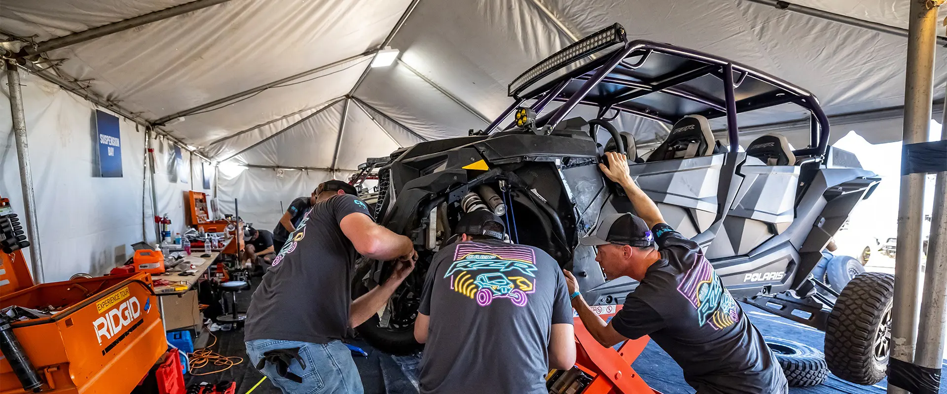 Camp RZR technicians service a black four-seat Polaris RZR inside a maintenance tent.