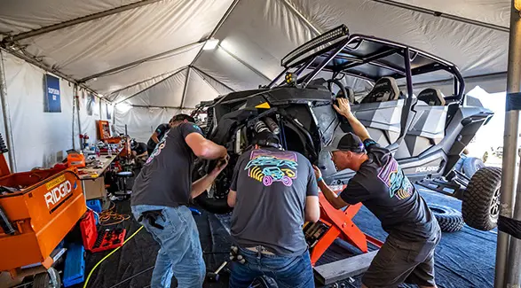 Camp RZR technicians service a black four-seat Polaris RZR inside a maintenance tent.