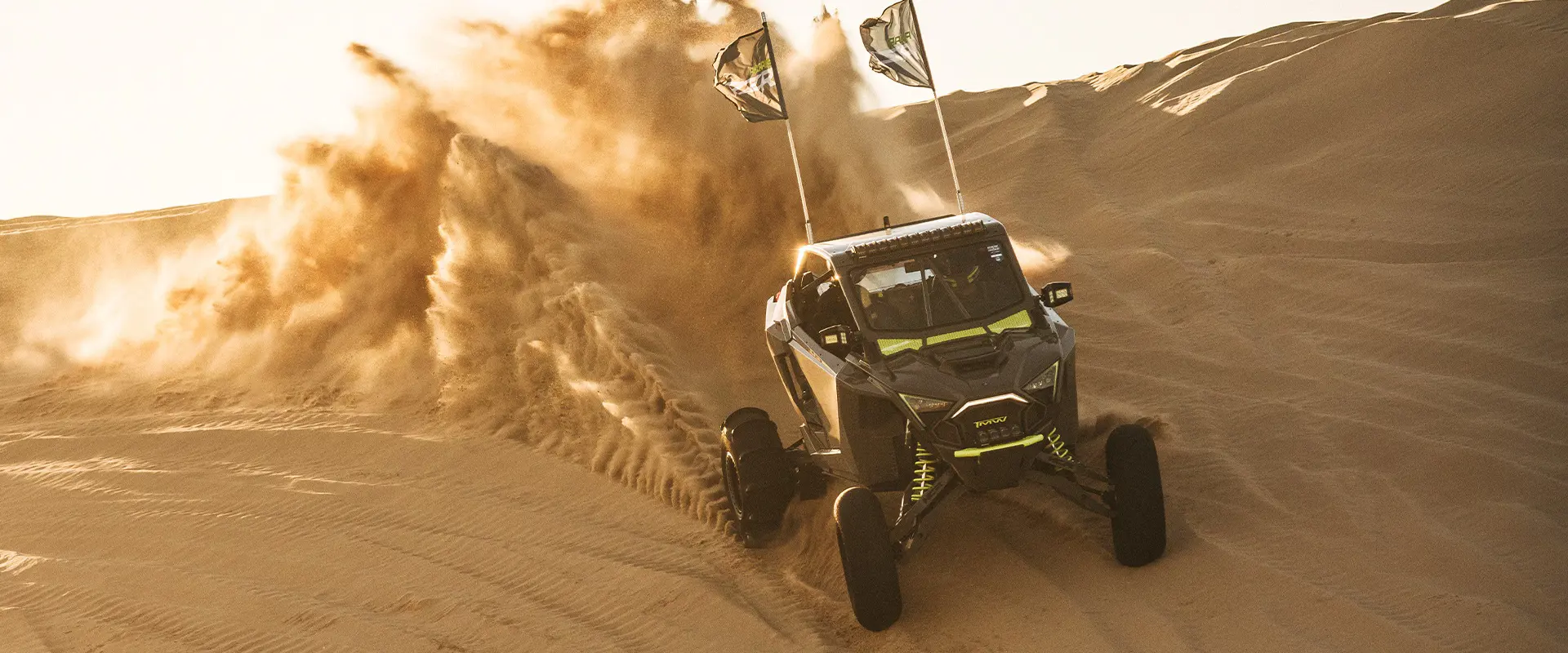 Polaris RZR SxS carving through desert dunes and spraying sand at sunset during Camp RZR.