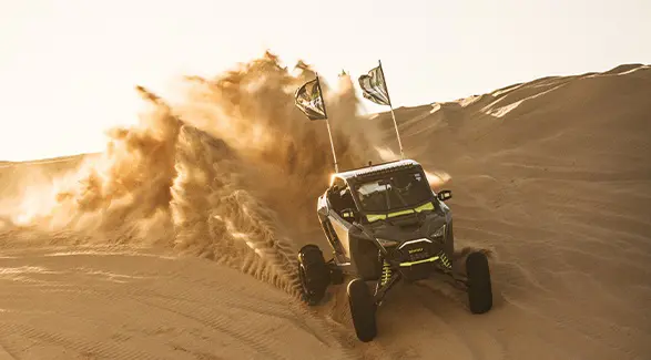 Polaris RZR SxS carving through desert dunes and spraying sand at sunset during Camp RZR.