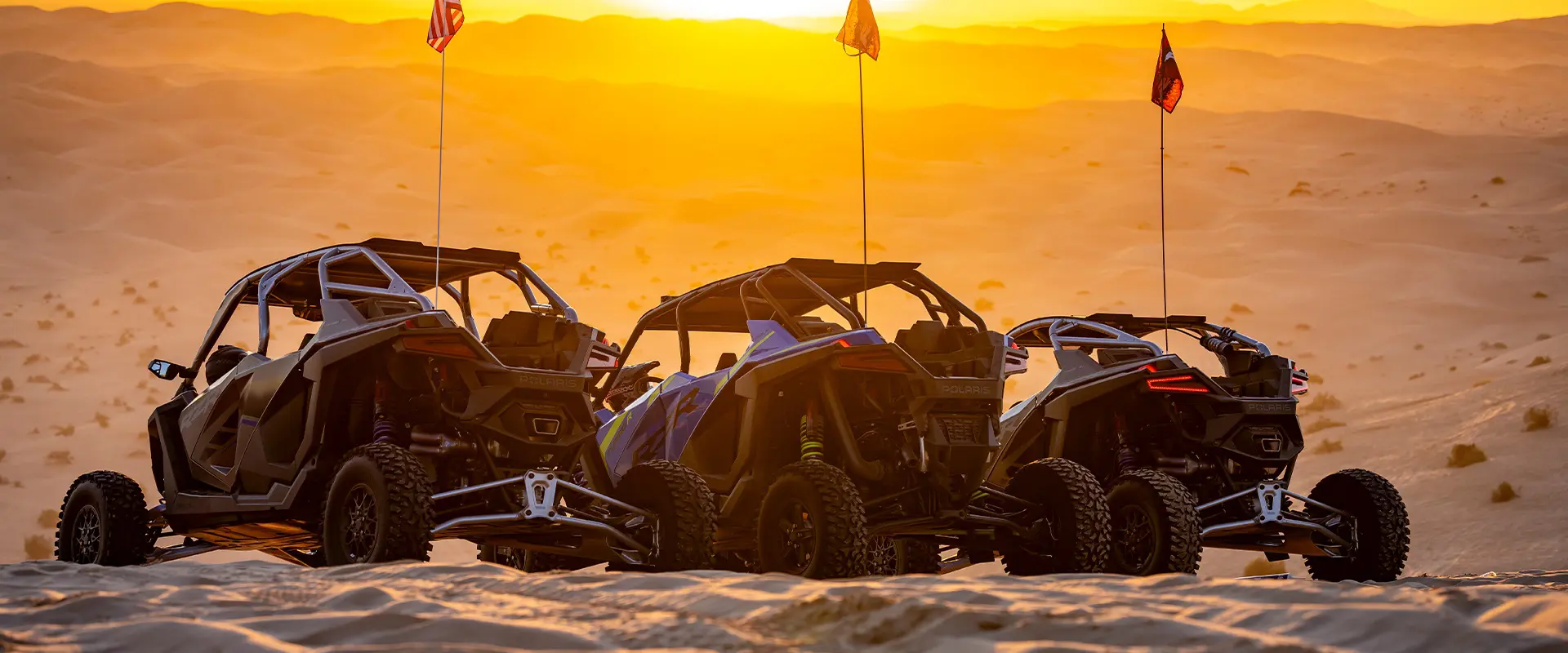 Three Polaris RZR side-by-sides parked on desert dunes beneath a golden sunset at Camp RZR.