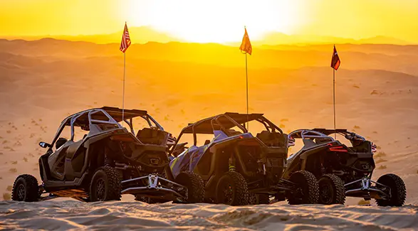 Three Polaris RZR side-by-sides parked on desert dunes beneath a golden sunset at Camp RZR.