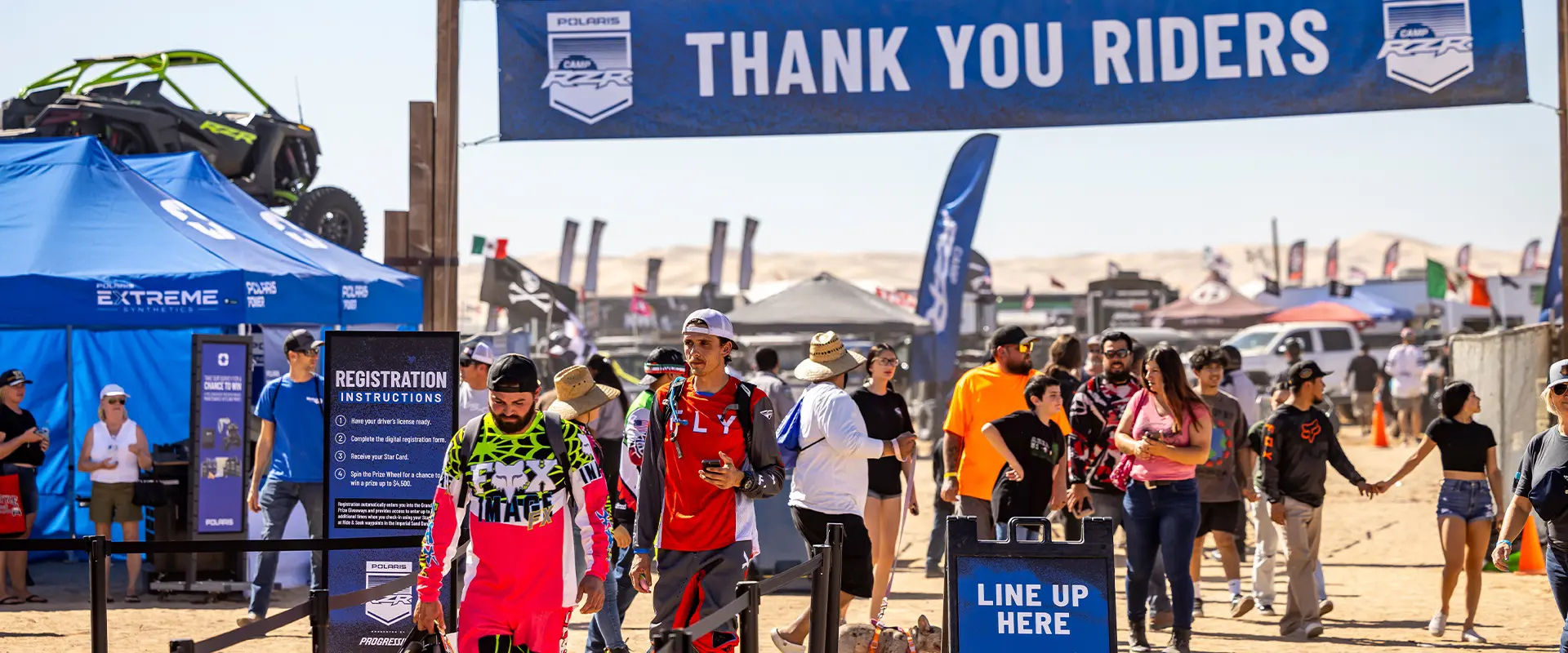 Attendees walking beneath a Thank You Riders banner at the Camp RZR registration area.