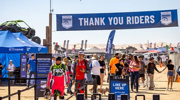 Attendees walking beneath a Thank You Riders banner at the Camp RZR registration area.