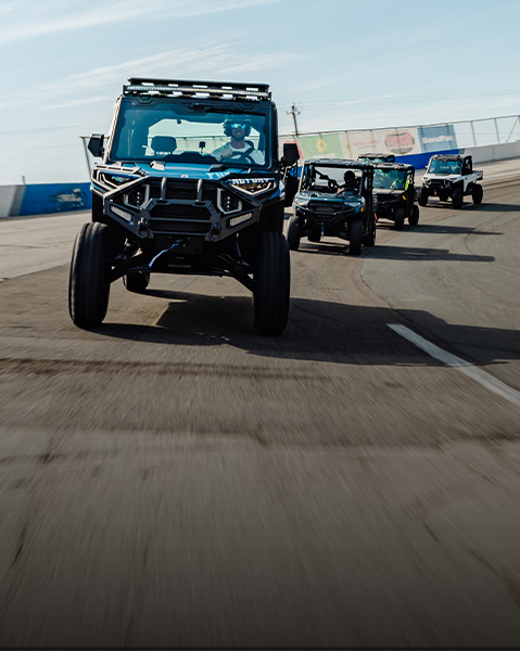 A convoy of Polaris UTVs led by a blue RANGER CREW XD 1500 NorthStar with Freedom Factory decals on a banked racetrack.