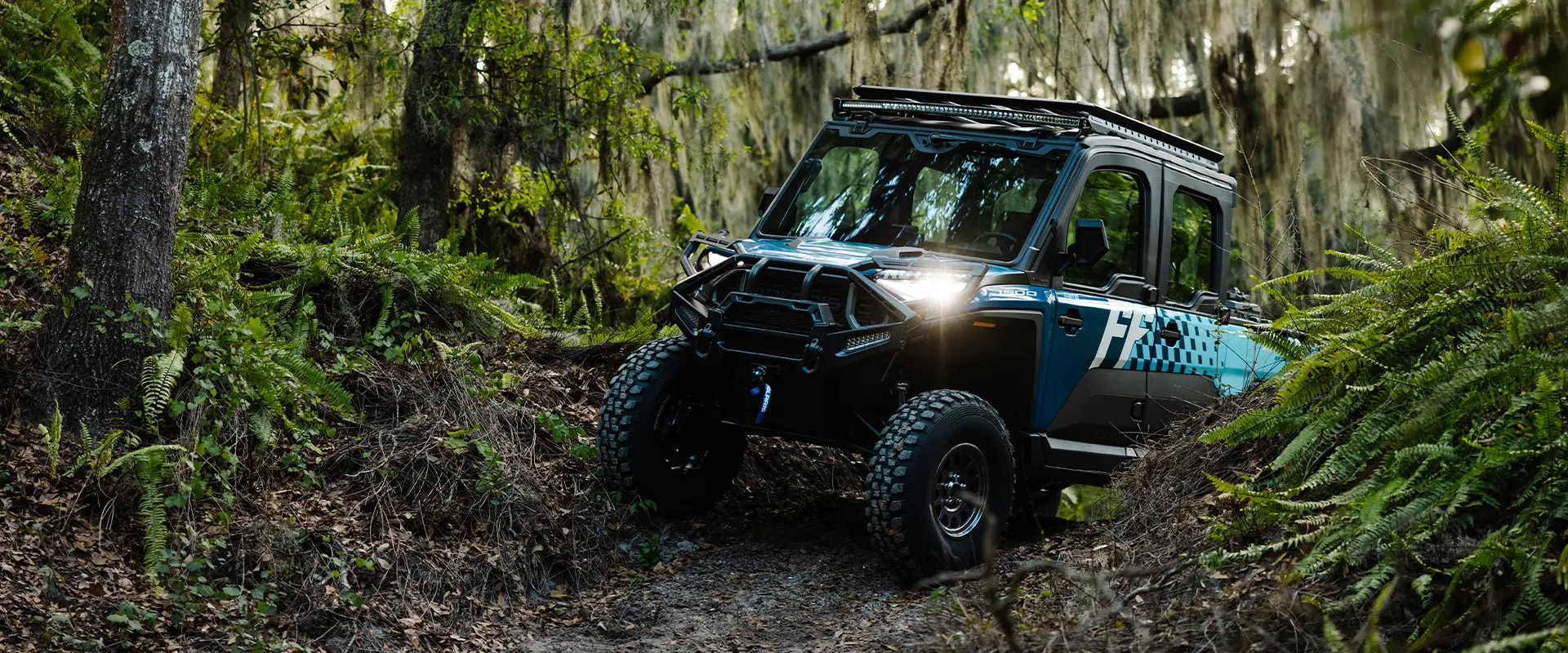 A blue Polaris RANGER CREW XD 1500 NorthStar with Freedom Factory branding navigates a swampy forest trail with Spanish moss.