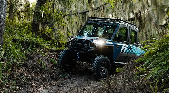 A blue Polaris RANGER CREW XD 1500 NorthStar with Freedom Factory branding navigates a swampy forest trail with Spanish moss.