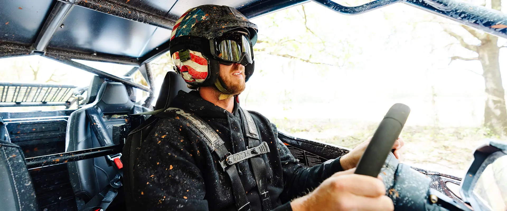 Cleetus McFarland in an American flag helmet drives a mud-splattered Polaris RZR PRO R 4 Ultimate.