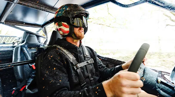 Cleetus McFarland in an American flag helmet drives a mud-splattered Polaris RZR PRO R 4 Ultimate.