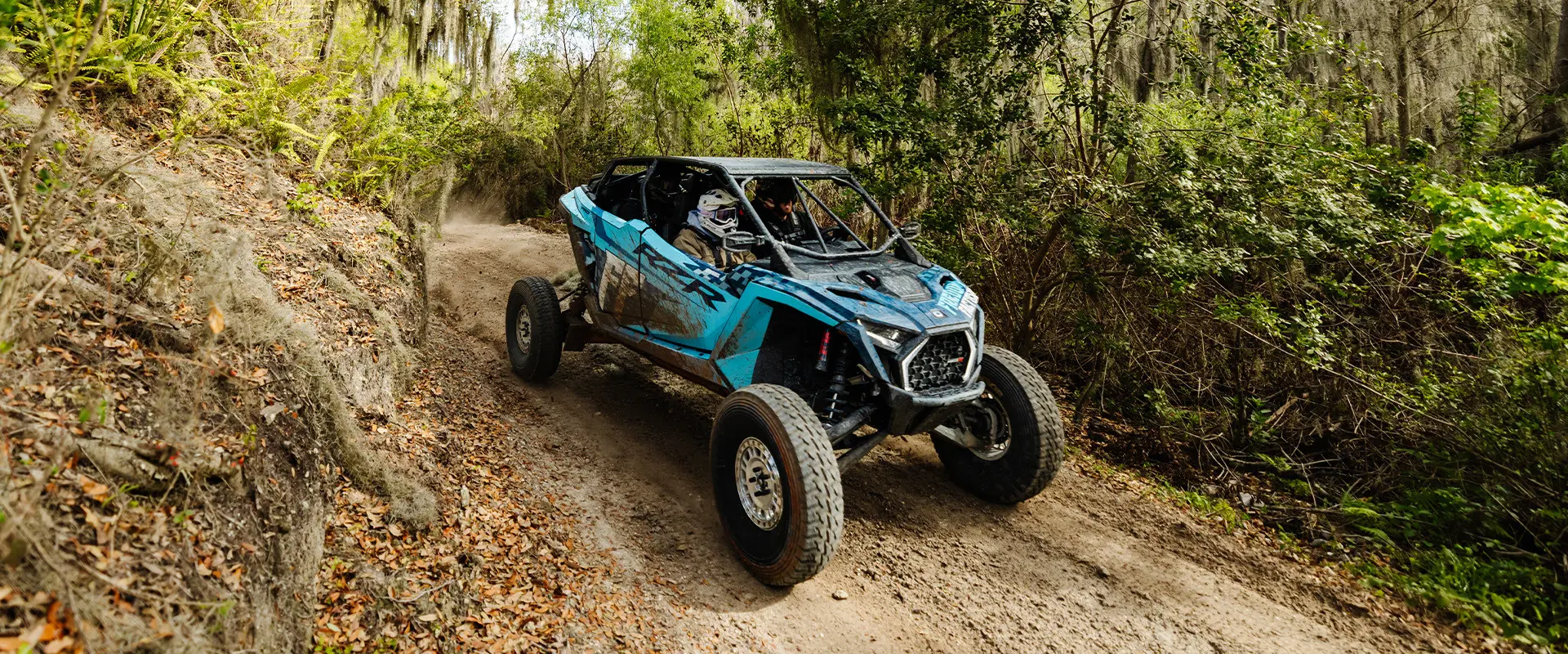 A blue Polaris RZR PRO R 4 Ultimate with Freedom Factory branding navigates a narrow, wooded dirt trail.