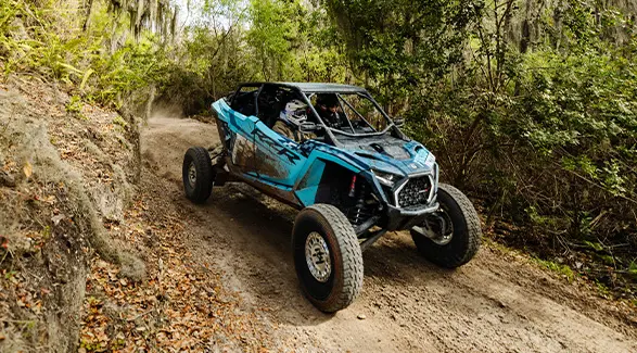 A blue Polaris RZR PRO R 4 Ultimate with Freedom Factory branding navigates a narrow, wooded dirt trail.