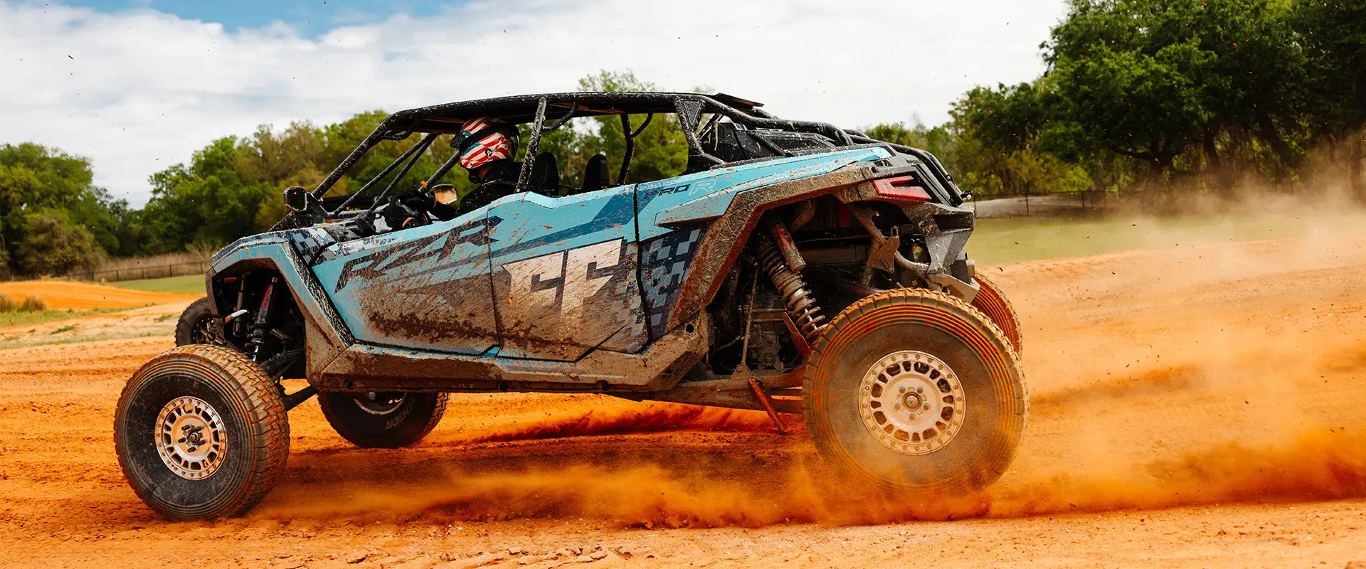 A blue Polaris RZR PRO R 4 Ultimate with the Freedom Factory logo kicks up a massive cloud of dust on a dirt track.