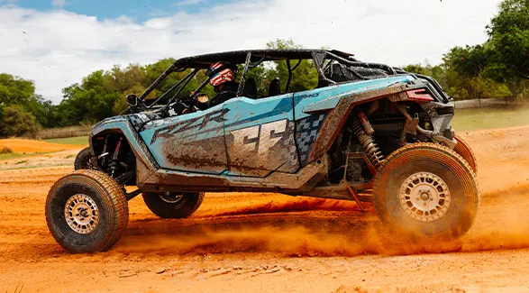 A blue Polaris RZR PRO R 4 Ultimate with the Freedom Factory logo kicks up a massive cloud of dust on a dirt track.