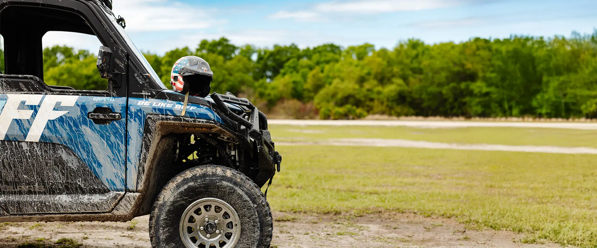 An American flag helmet rests on a mud-splattered blue Polaris RANGER CREW XD 1500 NorthStar with Freedom Factory decals.