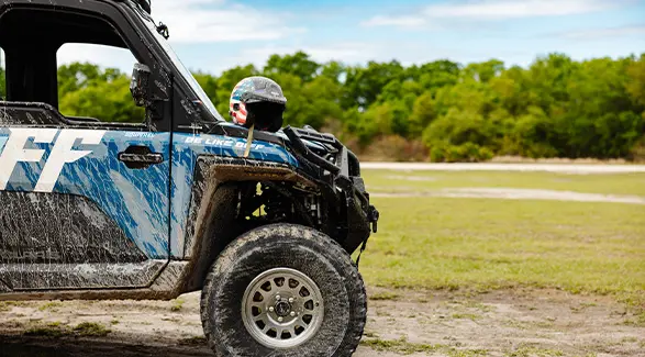 An American flag helmet rests on a mud-splattered blue Polaris RANGER CREW XD 1500 NorthStar with Freedom Factory decals.