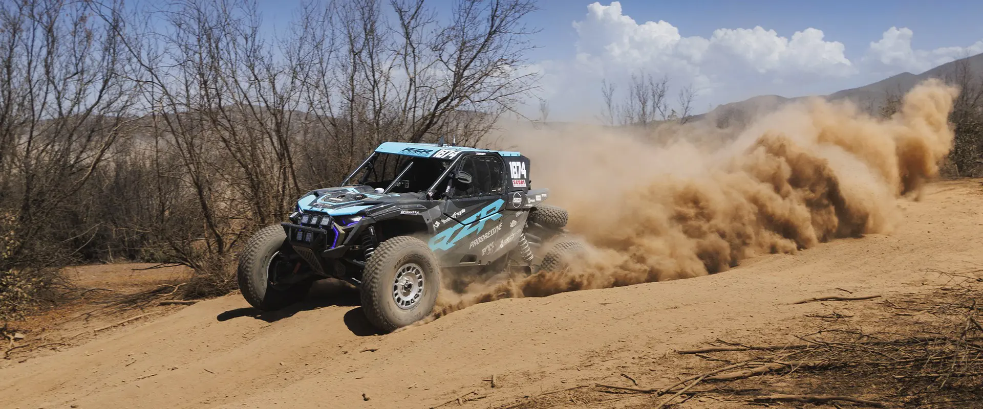 2025 Polaris RZR Pro R Factory side-by-side racing on a dusty trail, kicking up sand in a dynamic action shot.