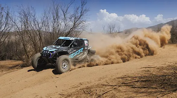 2025 Polaris RZR Pro R Factory side-by-side racing on a dusty trail, kicking up sand in a dynamic action shot.