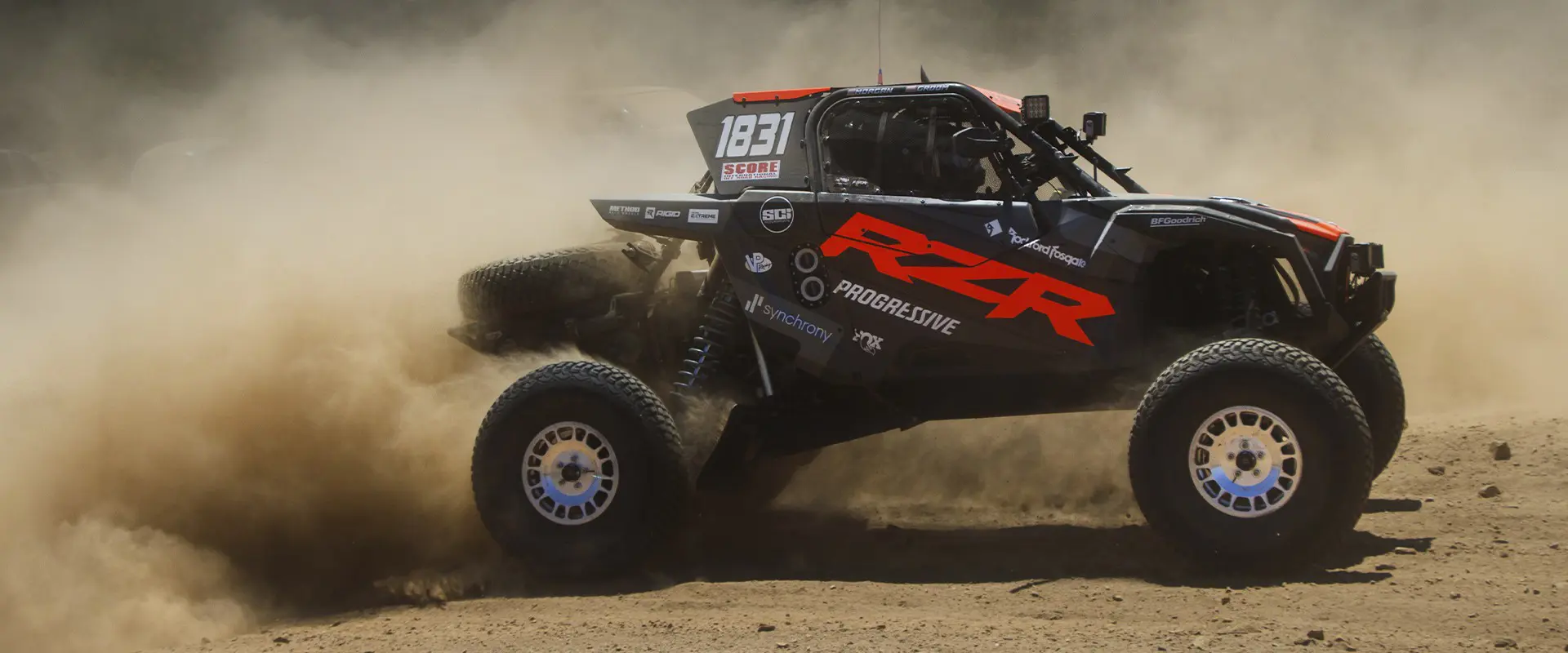 Side profile of a 2025 Polaris RZR Pro R Factory side-by-side driving on a rocky trail.