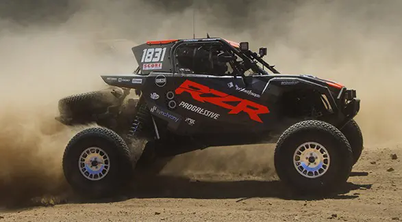 Side profile of a 2025 Polaris RZR Pro R Factory side-by-side driving on a rocky trail.