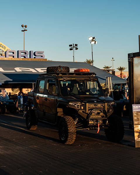 Polaris XPEDITION XP Side-by-Side displayed at an outdoor event booth with roof rack gear, parked near a Polaris tent and other off-road vehicles.