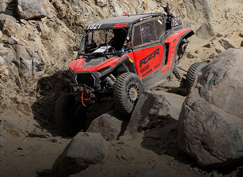 Polaris RZR Pro R Factory Side-by-Side rock crawling through a narrow canyon, navigating large boulders with suspension flex on rugged terrain.