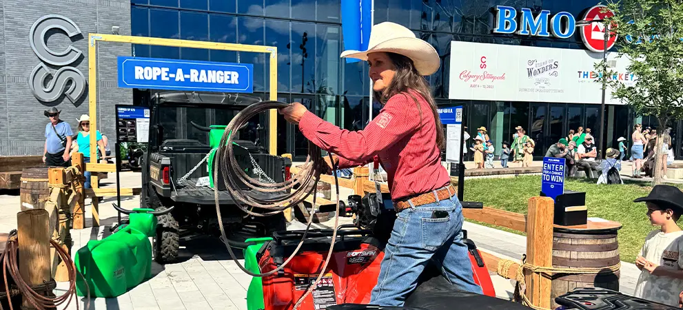 Participant on a Sportsman ATV practicing lasso skills at a Rope-A-Ranger setup, with a Polaris RANGER UTV behind and event signage.