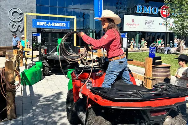 Participant on a Sportsman ATV practicing lasso skills at a Rope-A-Ranger setup, with a Polaris RANGER UTV behind and event signage.