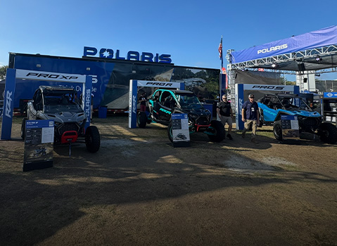 Polaris RZR Pro XP and Polaris RZR Pro R Side-by-Side vehicles on display at an outdoor event booth with branded signage and product stands.