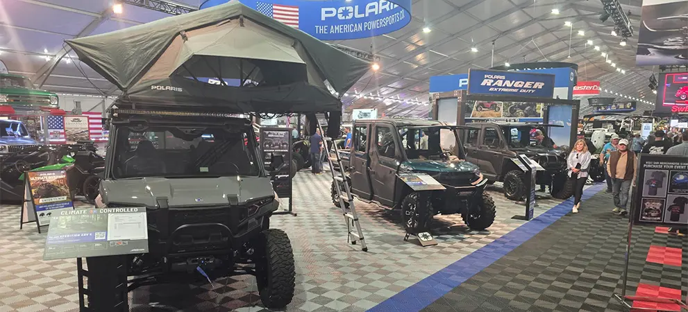 Polaris RANGER UTV lineup inside an event tent, including a model with a rooftop tent, displayed alongside visitors and product showcases.