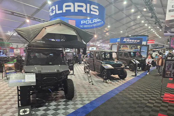 Polaris RANGER UTV lineup inside an event tent, including a model with a rooftop tent, displayed alongside visitors and product showcases.