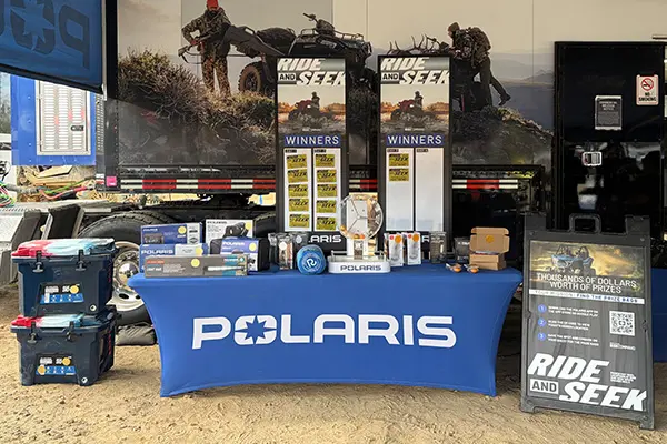 Polaris branded table displaying gear and prizes for a Ride and Seek promotion, set up in front of a trailer with signage and equipment.