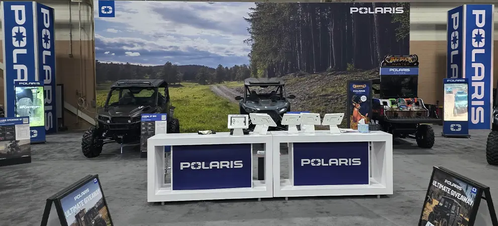Indoor Polaris booth with a Polaris RZR Side-by-Side and Polaris GENERAL Side-by-Side behind a registration counter with tablets and brand signage.