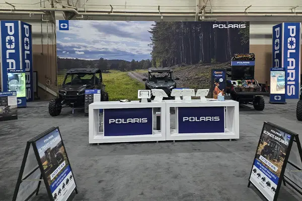 Indoor Polaris booth with a Polaris RZR Side-by-Side and Polaris GENERAL Side-by-Side behind a registration counter with tablets and brand signage.