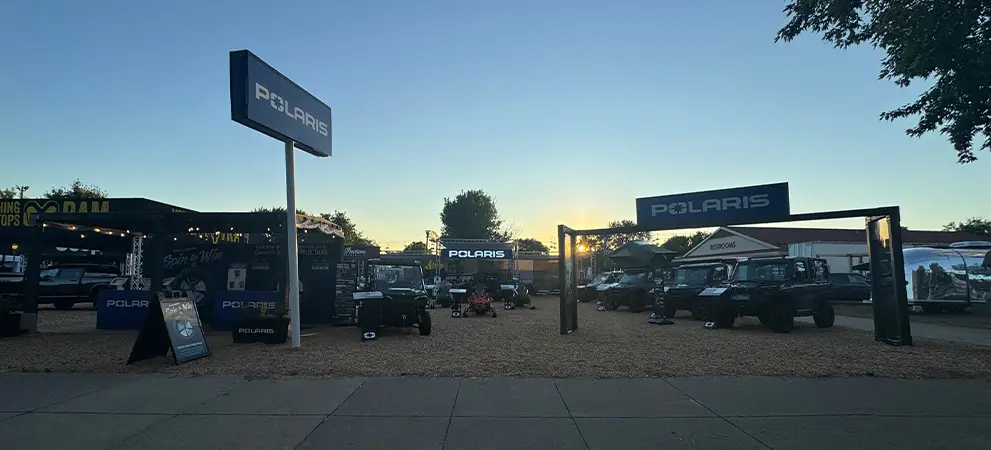 Polaris outdoor event entrance at sunset with multiple Polaris RANGER UTVs and off-road vehicles displayed under branded signs and tents.
