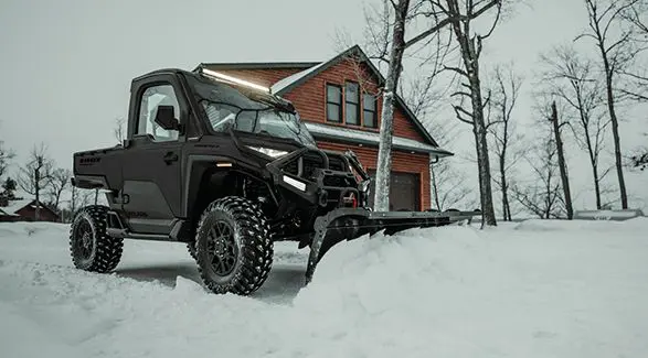 An enclosed cab 3-seater UTV plowing snow in the winter.