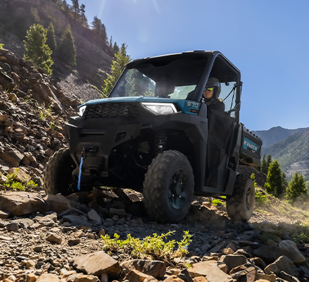 A Polaris RANGER SP 570 UTV navigates a steep, rocky mountain trail overlooking a vast valley with pine trees and high peaks.