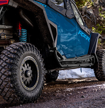 A Polaris RZR SxS with Pro Armor Crawler XP tires is stopped on a muddy road.