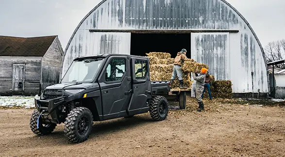 Farmers loading square bales onto a trailer pulled by a 2026 Polaris RANGER CREW XP 1000 NorthStar Edition UTV.