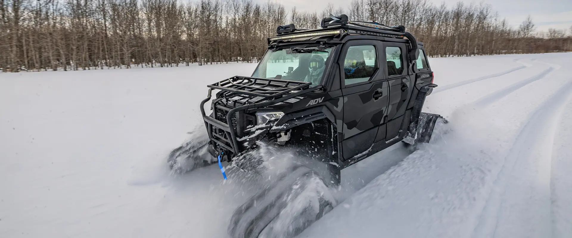 2026 Polaris XPEDITION ADV 5 NorthStar side-by-side with tracks installed driving in a snow-covered field.