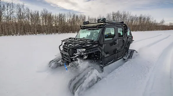 2026 Polaris XPEDITION ADV 5 NorthStar side-by-side with tracks installed driving in a snow-covered field.