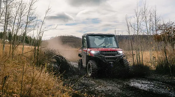 A 2026 Polaris RANGER XP 1000 NorthStar Edition cabbed UTV cruising through a muddy trail.