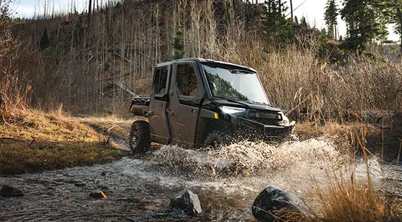 A 2026 Polaris RANGER CREW XP 1000 NorthStar Edition UTV power through a ravine while the riders sit dry and comfortable in the all-season cab.