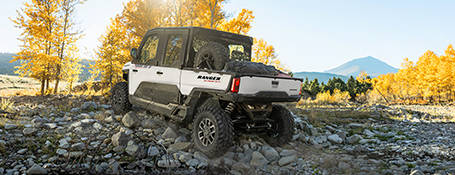 A white four-door fully-cabbed 2025 extreme duty UTV conquering rocky terrain.