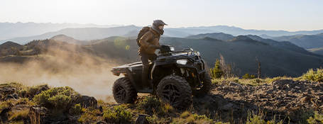 A person riding a black and red single seat 2025 sport ATV on a rugged mountain trail.