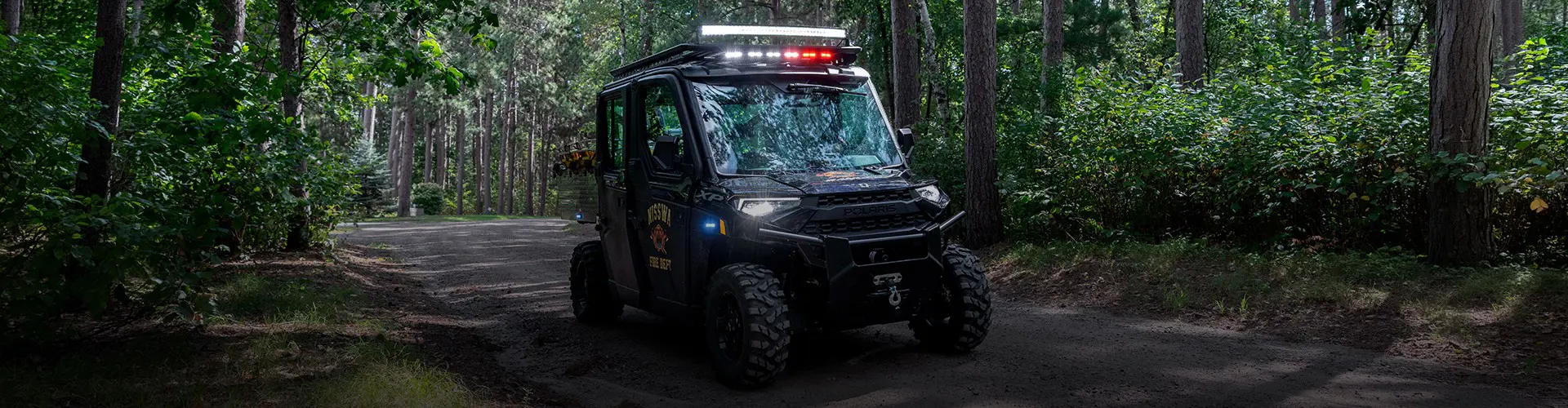 Polaris RANGER XP 1000 fire rescue side-by-side with emergency lights traveling along a wooded dirt trail.