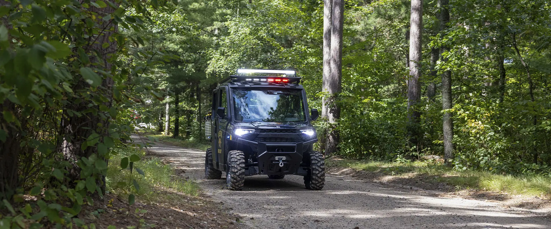 Polaris RANGER emergency response UTV travels along a narrow dirt road through dense Minnesota woods.