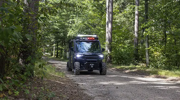 Polaris RANGER emergency response UTV travels along a narrow dirt road through dense Minnesota woods.